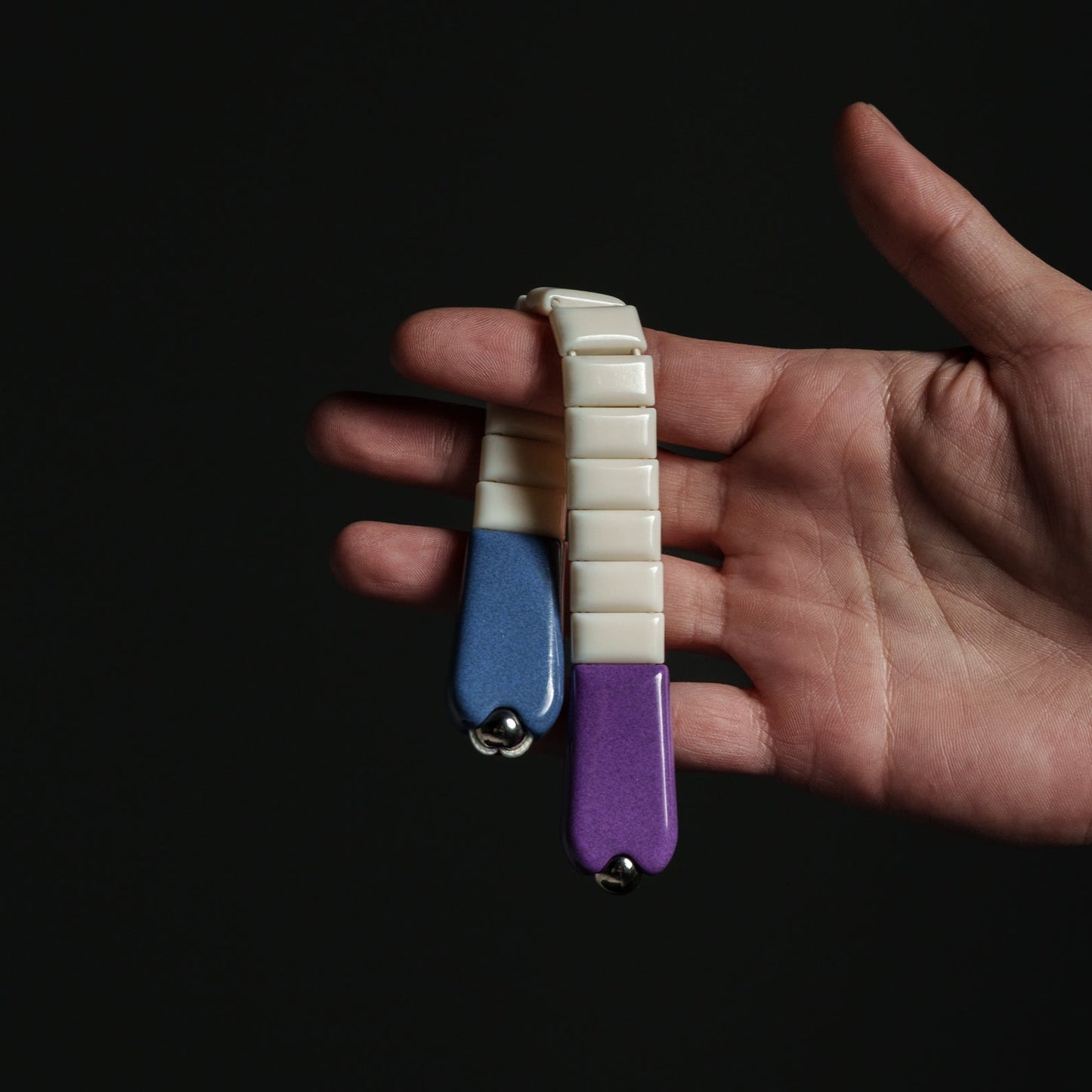 Hand holding a small, multicolored chetki against a dark background