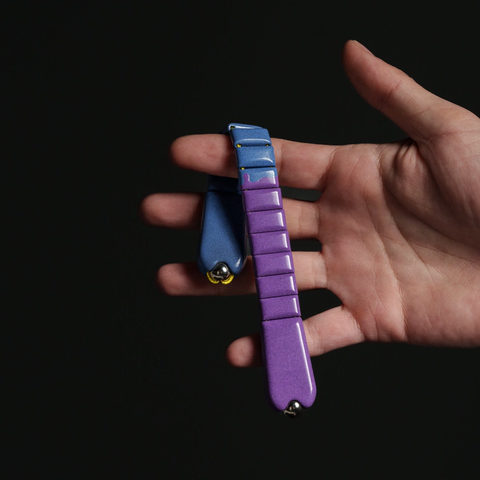 Hand holding a purple and blue chetki against a black background