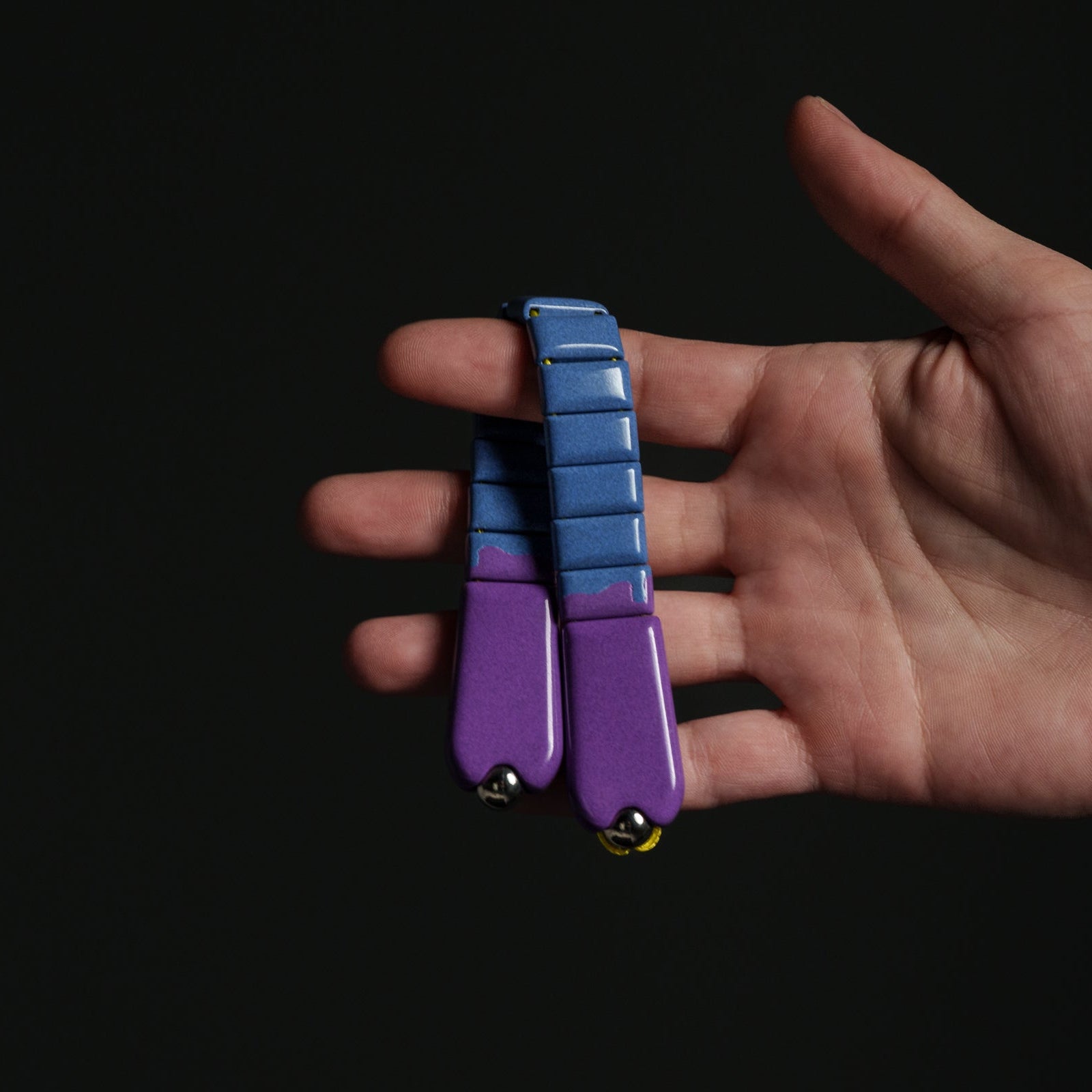 Hand holding a purple and blue chetki against a black background