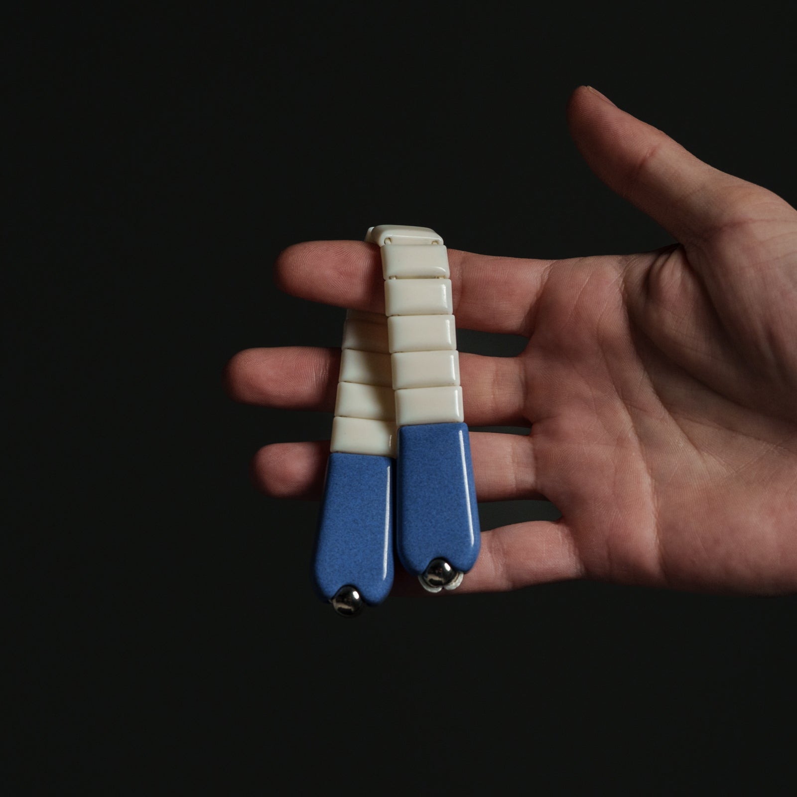 Hand holding a small blue and white chetki against a black background