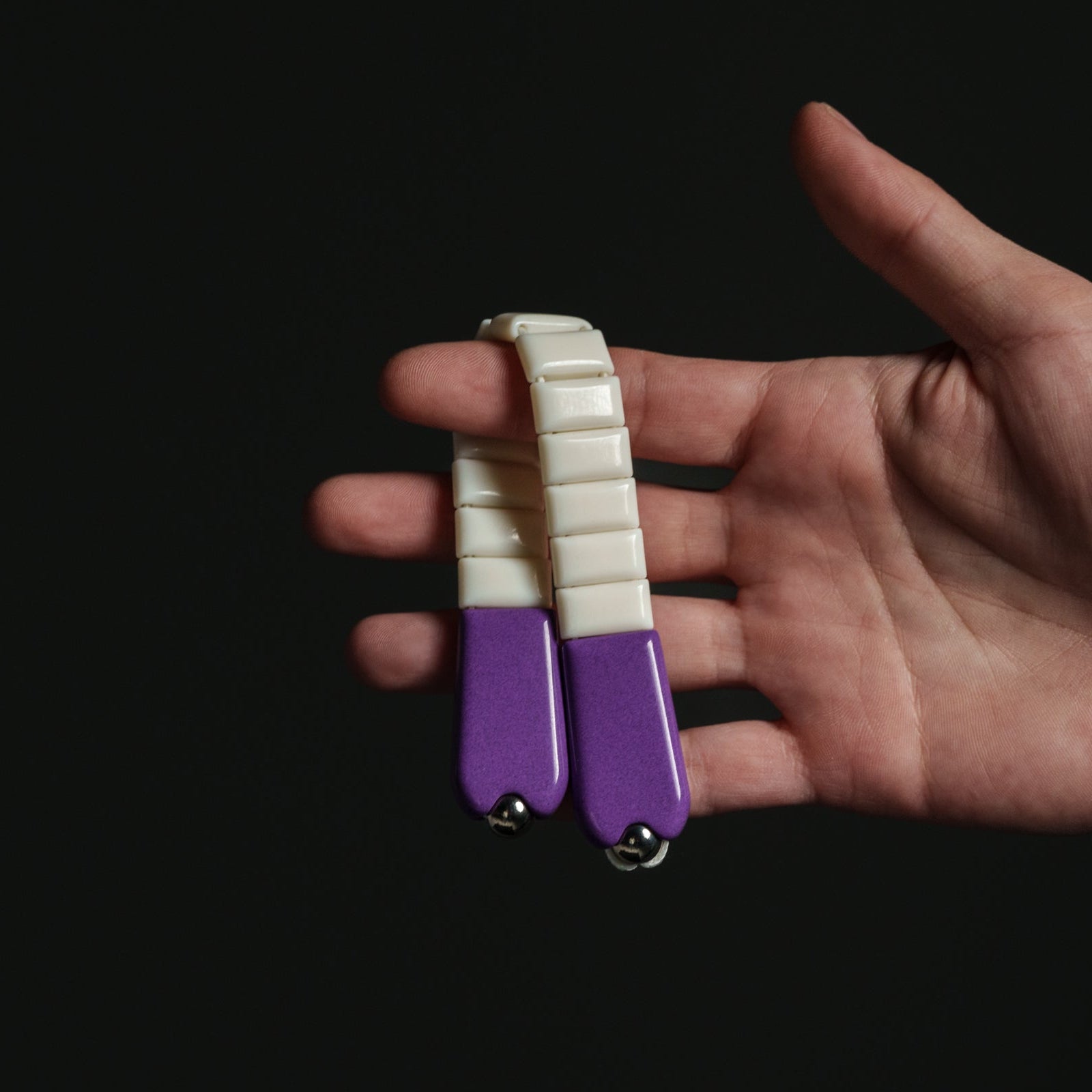 Hand holding a small purple and white chetki against a black background