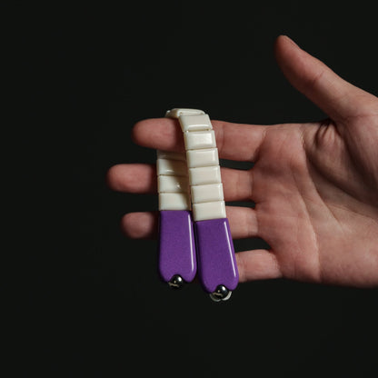 Hand holding a small purple and white chetki against a black background