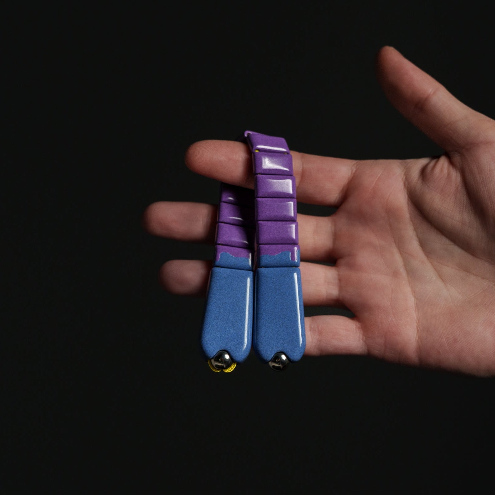 Hand holding a blue and purple chetki against a black background